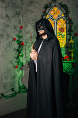 A guy in a black mask in the form of a skull and in a black cloak. Evil sorcerer with a magic wand. Wizard in the castle