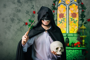 A guy in a black mask in the form of a skull and in a black cloak. Evil sorcerer with a magic wand...