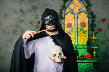A guy in a black mask in the form of a skull and in a black cloak. Evil sorcerer with a magic wand...