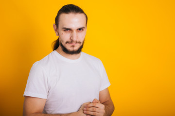 A guy with a beard in a white T-shirt on yellow folded his hands in the castle. Closed pose. Holding a fist