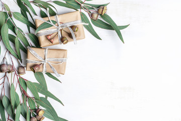 Gifts wrapped in natural paper with silver ribbon & rustic twine surrounded by eucalyptus leaves & gum nuts on white background. Celebration gifts for Birthday, Christmas, Mothers Day or Anniversary.