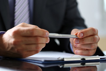 Male arm in suit and tie fill form clipped to pad with silver pen closeup. Sign gesture, read pact, sale agent, bank job, make note, loan credit mortgage investment, finance chief, legal law concept