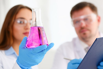 Female technician arms in protective gloves hold fluid sample bottle closeup. Medical worker in...