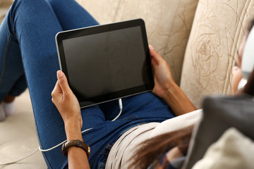 Female hand holds black tablet pad in home setting while sitting on couch engaged an blogger...
