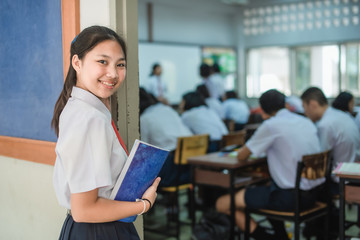 An Asian female high school student in white uniform is turning her face and smiling while walking into the classroom.