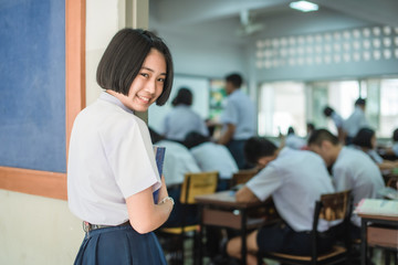 An Asian female high school student in white uniform is turning her face and smiling while walking into the classroom.