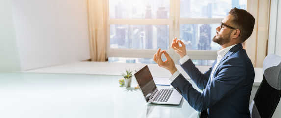 Businessman Sitting Behind Desk Meditating In Office