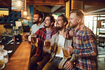 A group of guys watching sports on tv in a pub bar.