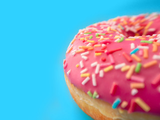 macro photo of a pink strawberry donut with sprinkles on a blue background