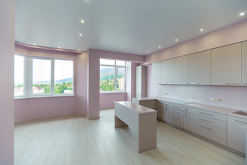 Fototapeta na wymiar A large room with pink walls and a white kitchen set. Kitchen furniture is new with all kitchen appliances. In front of the kitchen is a white table. Fresh, new renovation.