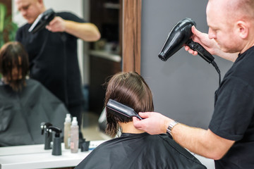 Hairstylist dries hair of woman.