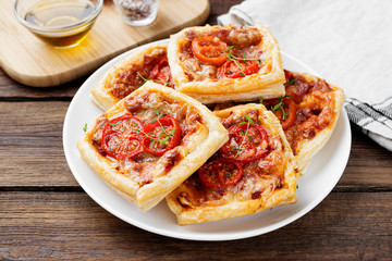 Puff pastry mini pies with cheese and tomatoes on wooden background