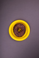 Chocolate donut on a yellow plate on a dark background. Abstraction and minimalism.