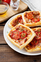 Puff pastry mini pies with cheese and tomatoes on wooden background
