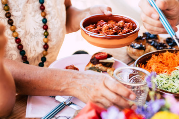 Close up with old senior hands taking food to eat from the table at home or restaurant - couple and friennds having lunch together with vegetariann and healthy menu