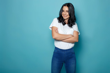 Young woman in the studio on a blue background conveys different emotions. Beautiful woman in jeans and a white t-shirt.