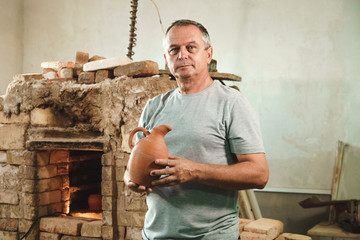 Master potter stands near pottery kiln and show his product.