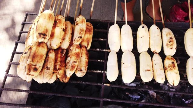 Close up shots of cardava banana on bbq fire stand with skewers.