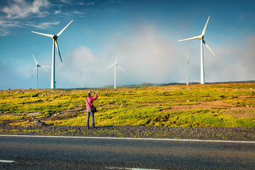 Fototapeta na wymiar Tourist takes a picture of wind turbines in the morning fog. Fantastic summer view of Faroe Islands, Kingdom of Denmark, Europe. Ecology concept background..