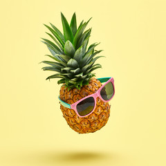 Flying in air pineapple tropical fruit on yellow. Minamal, Vitamin pineapple in sunglasses. Whole sweet fresh fruit. Levitation, falling fly pineapple creative concept