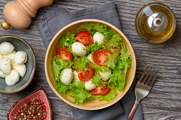 Fresh salad with cherry tomatoes, mozzarella cheese, greens leaves in bowl. Healthy summer salad vegetarian meal concept. Tomatoes and lettuce home made caprese salad on wood, top view