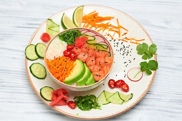 Hawaii salmon poke, avocado, rice, seaweed, cucumber, radish, carrot in bowl. Home made vegetarian poke. Seafood concept. Asian salmon poke salad on white wood background.