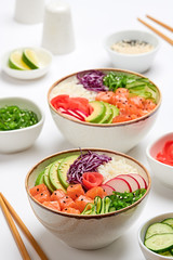 Hawaii salmon poke, avocado, rice, seaweed, cucumber, radish, carrot in bowl. Home made vegetarian poke. Seafood concept. Asian salmon poke salad on white background.