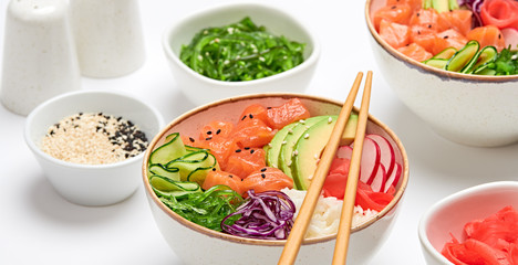 Hawaii salmon poke, avocado, rice, seaweed, cucumber, radish, carrot in bowl. Home made vegetarian poke. Seafood concept. Asian salmon poke salad on white background.