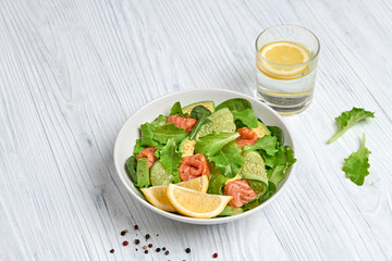 Salmon salad, cucumber, spinach, lollo, lettuce. Home made vegetarian salmon salad. Seafood tasty diet concept. Mix leaves greens with salmon fish in plate on white wood background.