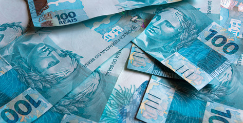 Fundo azul com cédulas de cem reais do Brasil