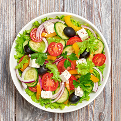 Greek salad with cucumeber, olives, feta cheese, cherry tomatoes, bell pepper, onion and lettuce. Diet, vitamin food. Tasty salad in bowl on wood, top view.