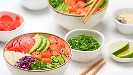 Hawaii salmon poke, avocado, rice, seaweed, cucumber, radish, carrot in bowl. Home made vegetarian poke. Seafood concept. Asian salmon poke salad on white background.