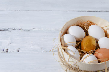 Easter background. In a sieve in the hay there are white chicken eggs, one golden egg, one brown. A...