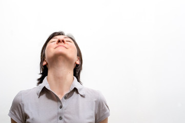 Portrait of a young happy brunette woman standing on a white wall, smiling with closed eyes in a peaceful manner. Positive human emotions.
