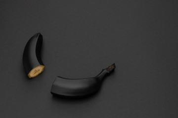 Two halves of a black banana on the matte black background. Minimal style. Conceptual minimalist black art. Matte surface. Cut fruit. One. Space for text