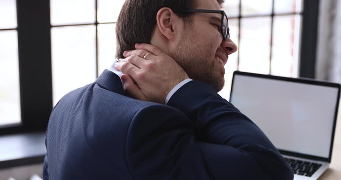 Tired businessman rubbing stiff neck tensed muscles having fibromyalgia problem. Fatigued of computer office worker feels backache after sedentary office work in uncomfortable chair. Closeup back view