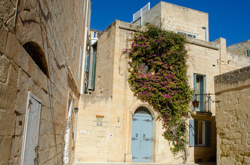 Fototapeta na wymiar Flowers over door of traditional stone house Mdina Malta