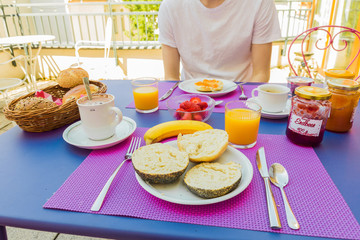 Homemade outdoor brunch with bagels & bread, fresh pressed orange juice & hot chocolate, jam, bio bananas & strawberries. Colorful table. POV shot. Berlin, Germany. 