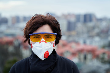 Coronavirus and pollution theme: young woman in respirator and goggles on a city background