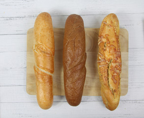 three baguettes on a cutting board on white wooden background flat lay. Horizontal image