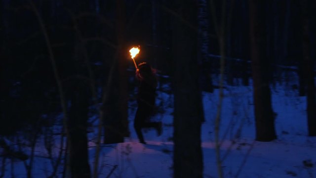 Young scared woman with torch running from something in the night forest