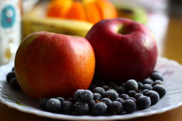  red apples and black currant berries on a white plate