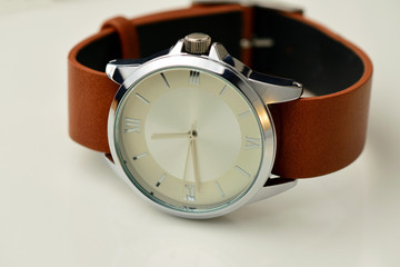 Silver wrist watch with a brown single-piece leather strap. Double-sided zulu or nato strap. White background.