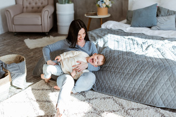 young mother is having fun playing with her little son on the floor near the bed