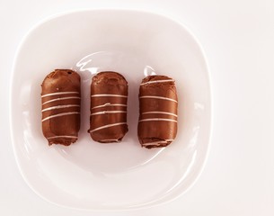On a white plate are three chocolate cakes with white icing. Cakes are fresh and sweet. The treat is called 