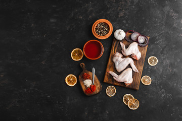Raw chicken wings with spices for cooking on a wooden cutting Board on a dark background. The view from the top. Side view. Space for text.