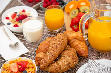 Breakfast Served in the morning with Fruit Yogurt, Butter croissant and corn flakes Whole grains and raisins with milk in cups and Strawberry, Raspberry, Kiwi, Fresh Orange Juice on breakfast table