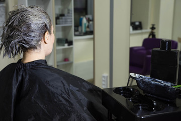 Client sitting in the chair in front of the mirror in beauty salon, waiting for the hair procedures with color mask