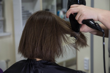 Naklejka premium Professional hairdresser drying woman's hair with hair dryer in beauty salon after beauty procedures and hair coloring