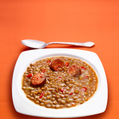 lentejas con chorizo u cuchara sobre fondo naranja. lentils with chorizo ​​u spoon on orange background.